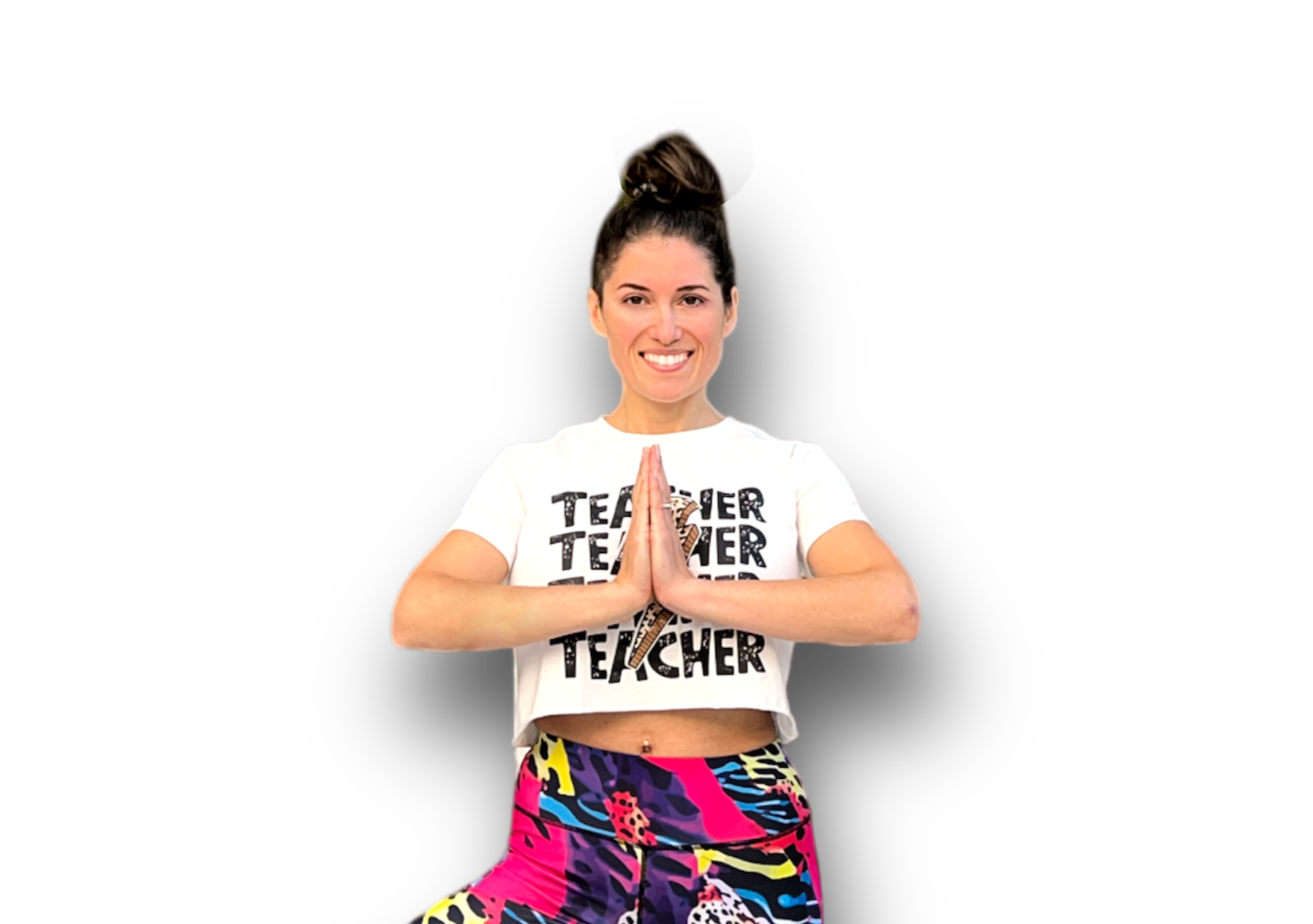 Contact professeur yoga Femme souriante les mains jointes avec un t-shirt portant le mot teacher et des pantalons de yoga colorés.